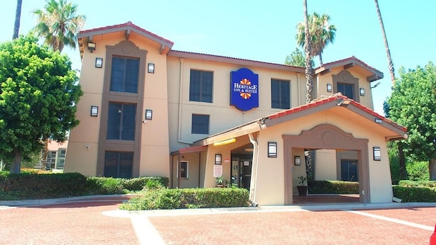 A Heritage Inn & Suites building with a beige facade, multiple windows, and a red roof. - Heritage Inn and Suits (San Bernardino)