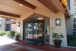 Entrada de un edificio con puerta de cristal, señal de advertencia y planta en maceta.
