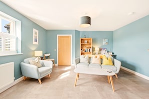 A living room with a light blue wall, a wooden door, a bookshelf, and two sofas. - 4 Brindles Manse - North East Escapes (North Sunderland)