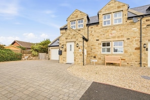 A stone building with a paved driveway, a bench, and a no parking sign. - 4 Brindles Manse - North East Escapes (North Sunderland)