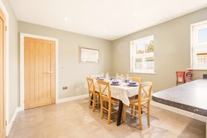 A dining area with a table set for six, wooden chairs, a framed picture on the wall, and a window with blinds. - 4 Brindles Manse - North East Escapes (North Sunderland)