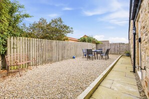 A patio with a table and chairs, a wooden fence, and a stone wall. - 4 Brindles Manse - North East Escapes (North Sunderland)