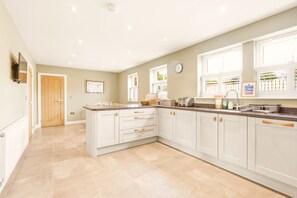A spacious kitchen with white cabinetry, a large island, and a window providing natural light. - 4 Brindles Manse - North East Escapes (North Sunderland)