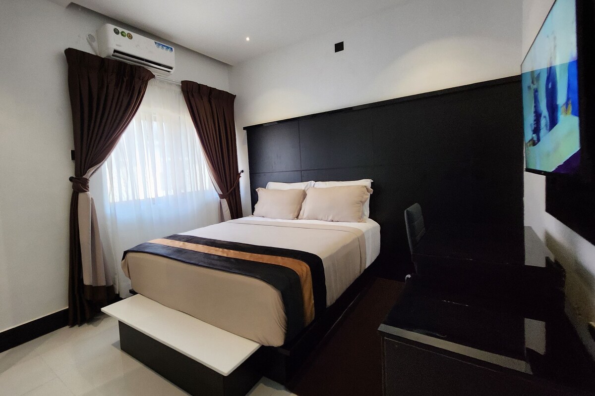A hotel room with a bed, a bench, a TV, and an air conditioning unit.