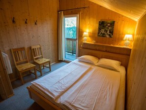 Quarto de cabana de madeira com cama, duas cadeiras, janela e varanda.
