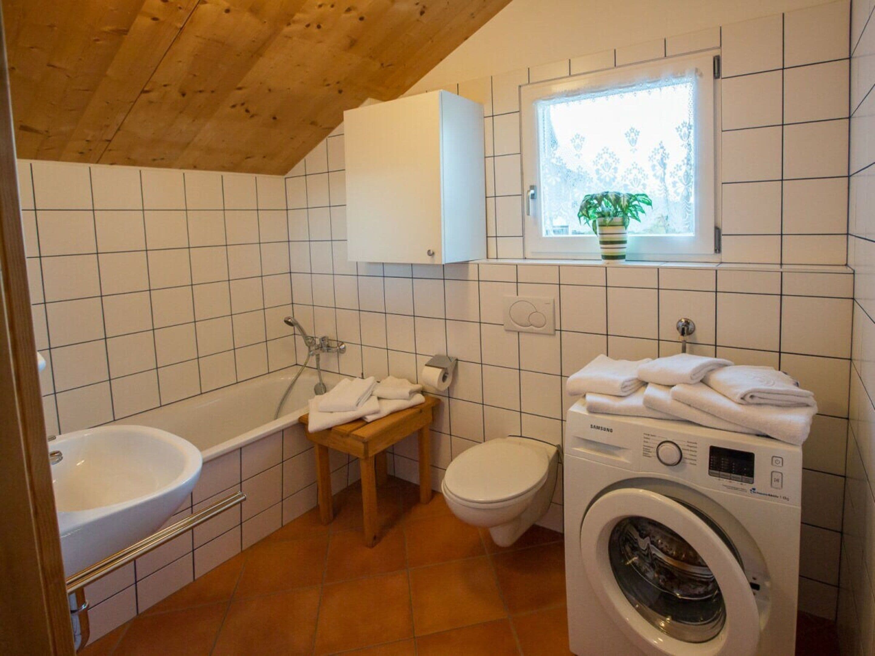 Ett litet badrum med badkar, toalett och tvättmaskin.