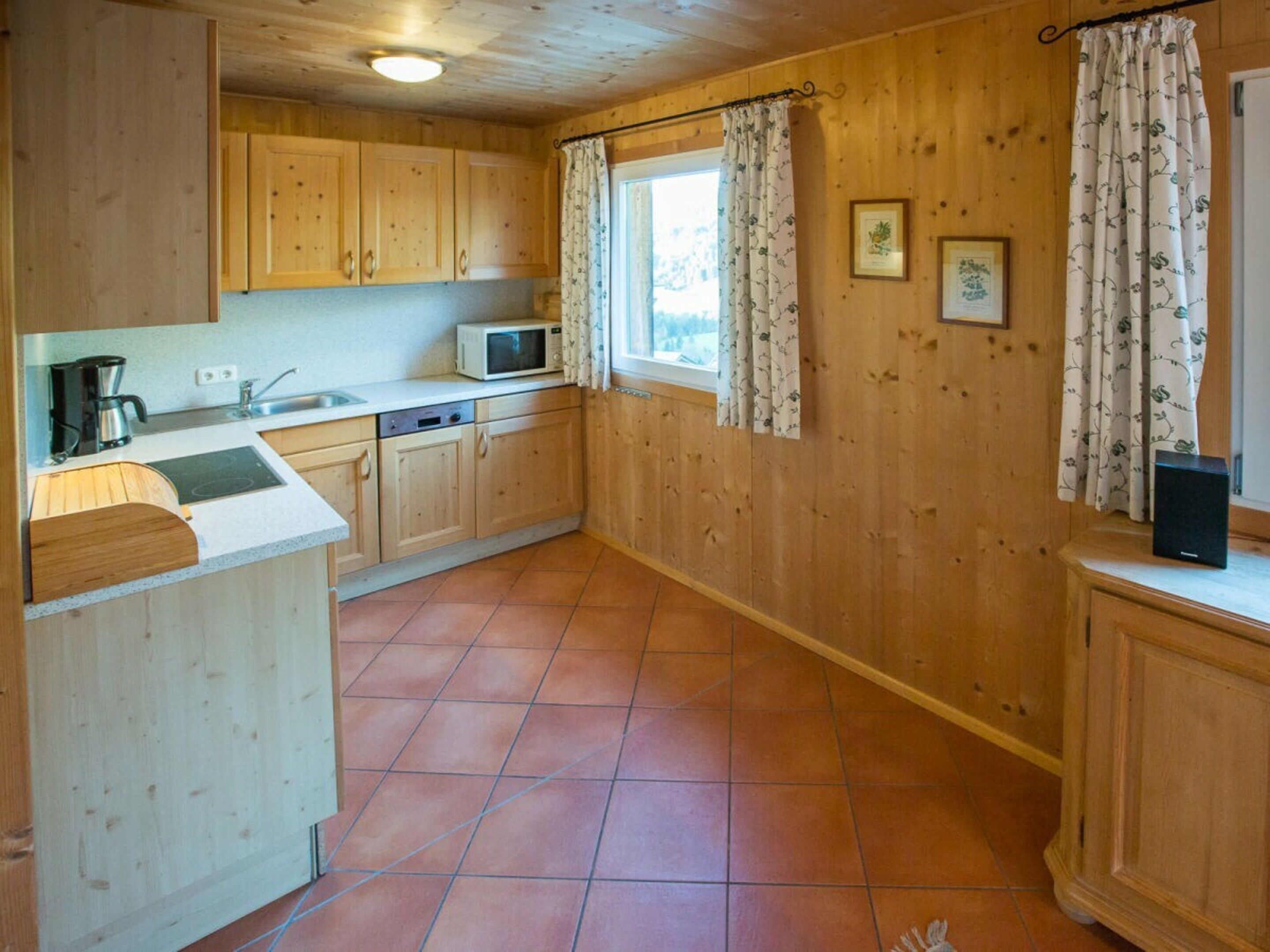 A kitchen with wooden cabinets, a microwave, a sink, and a window with curtains.