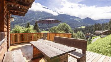 A wooden deck with a picnic table and chairs, overlooking a mountainous landscape.