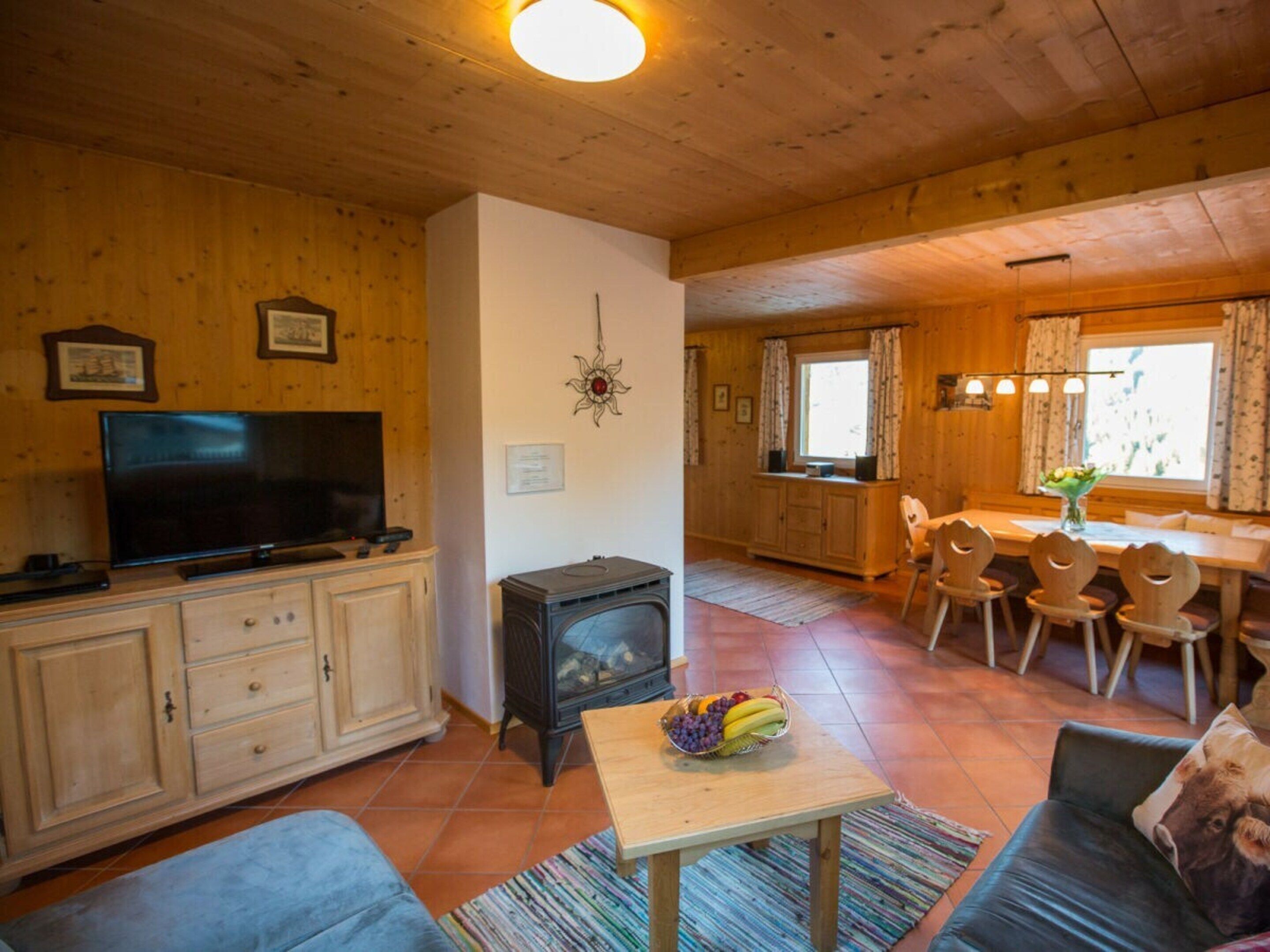 A cozy cabin interior with a television, wooden cabinets, a fireplace, a dining area with chairs, and a sofa.
