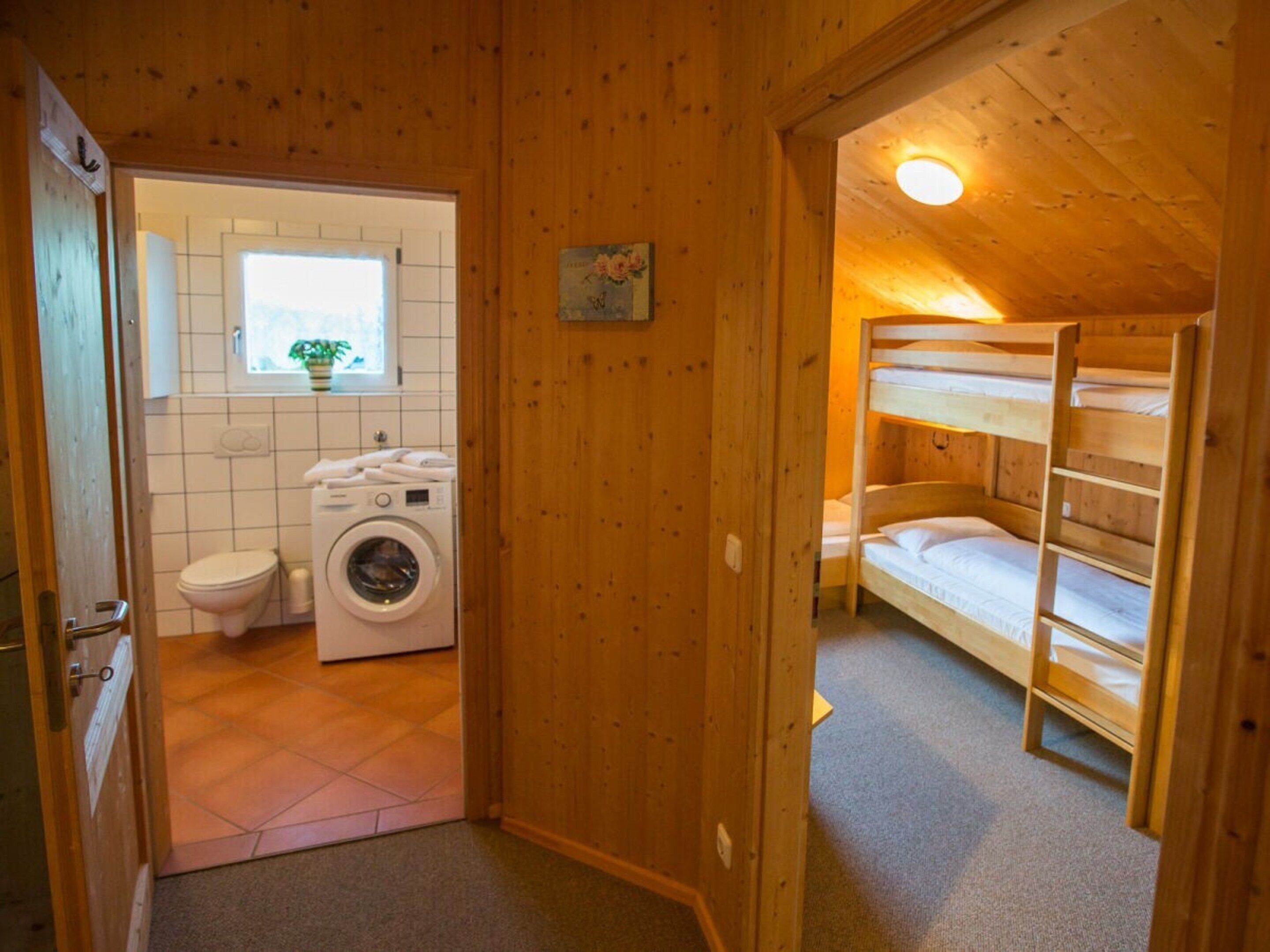 Een houten interieur met een wasmachine, toilet en stapelbedden.