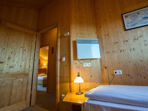 Quarto de cabana de madeira com cama, mesa com abajur, ar-condicionado e mapa emoldurado na parede.