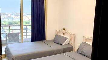 A hotel room with two beds, a large window with curtains, and a ceiling light fixture.