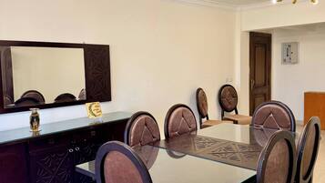 A dining area with a glass-top table, six upholstered chairs, a decorative mirror, and a ceiling light fixture.