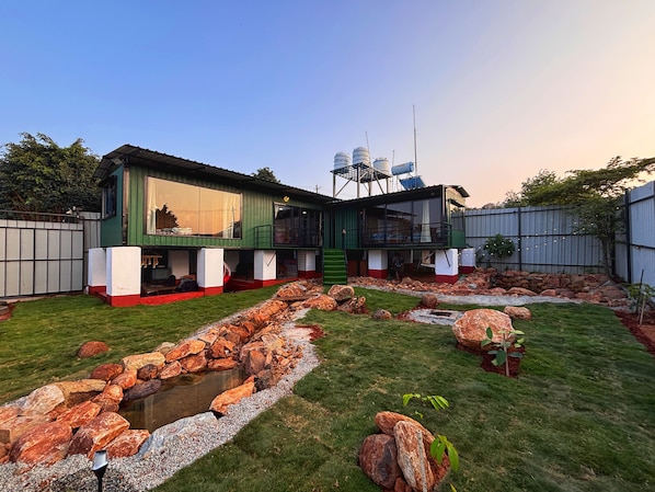 Uma casa moderna com fachada verde e branca, um caminho de pedra e um pequeno lago.