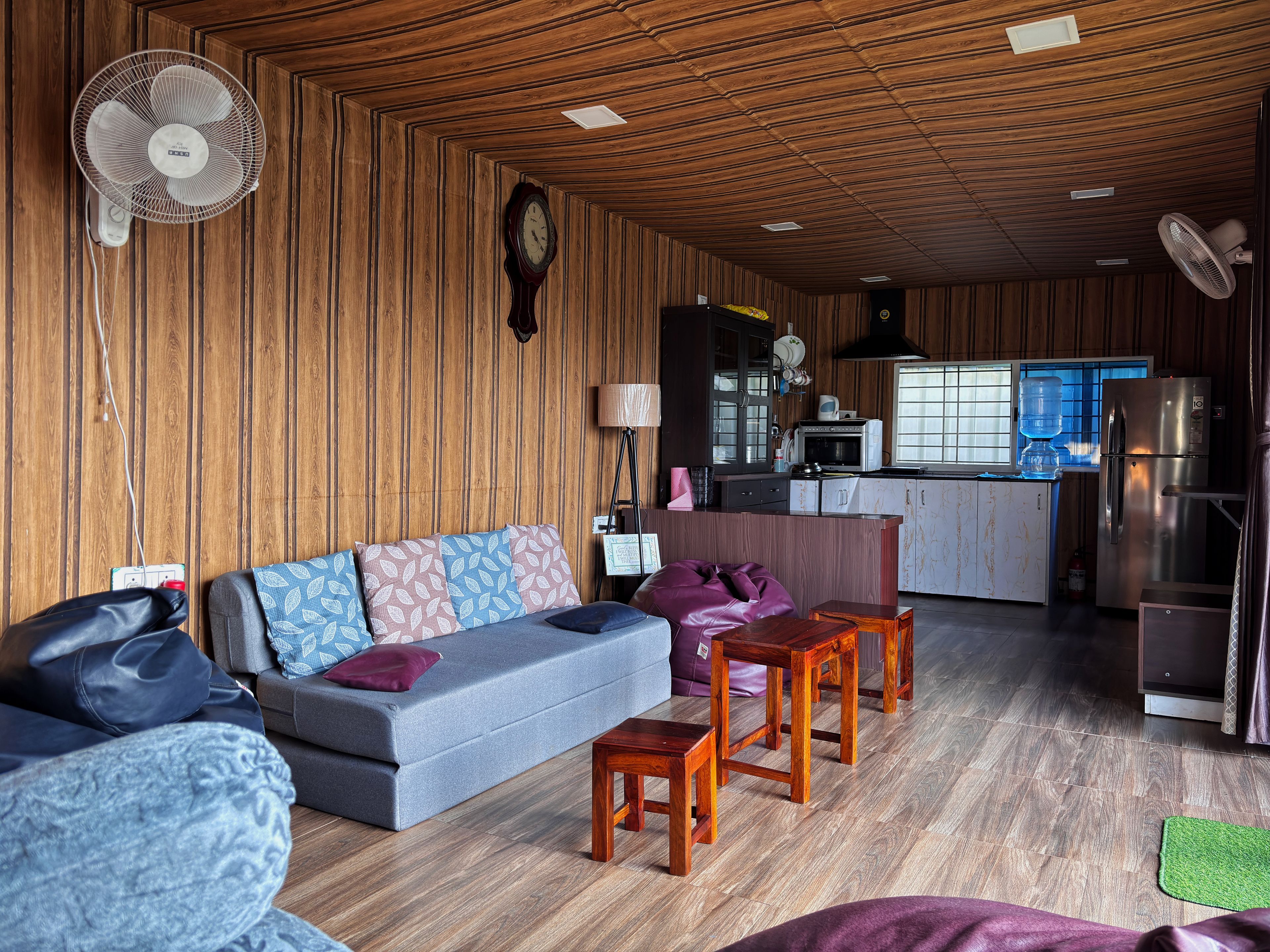 A compact living space with a sofa, chairs, a small kitchen area, and a wooden ceiling.