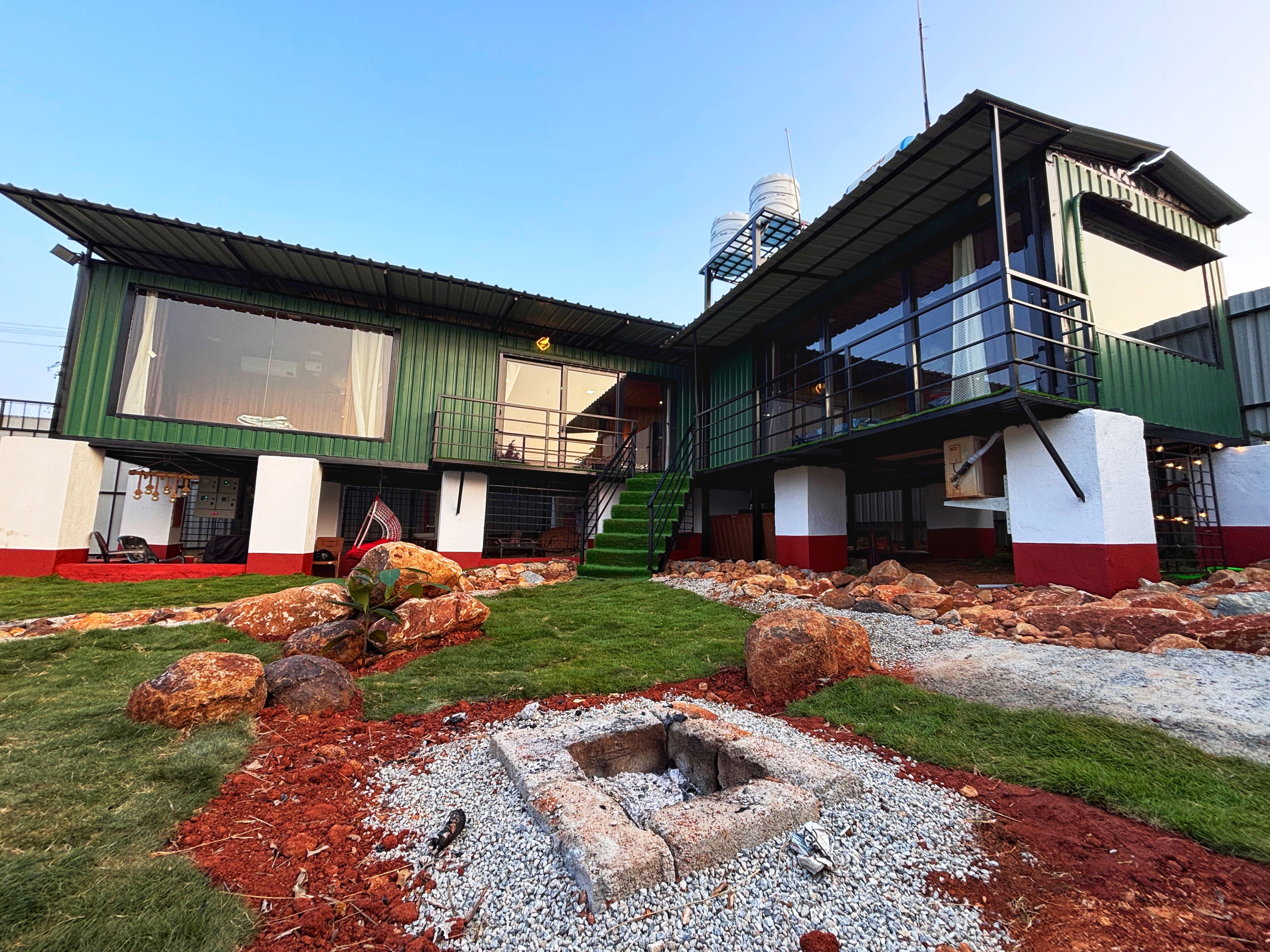 A two-story building with a green and white facade, a visible staircase, and a small garden area with rocks and gravel.