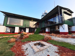 Edifício de dois andares com fachada verde e branca, escadaria visível e pequena área de jardim com pedras e cascalho.