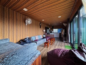 Quarto com teto de madeira, sofá, cama, cadeira e uma área de cozinha compacta.