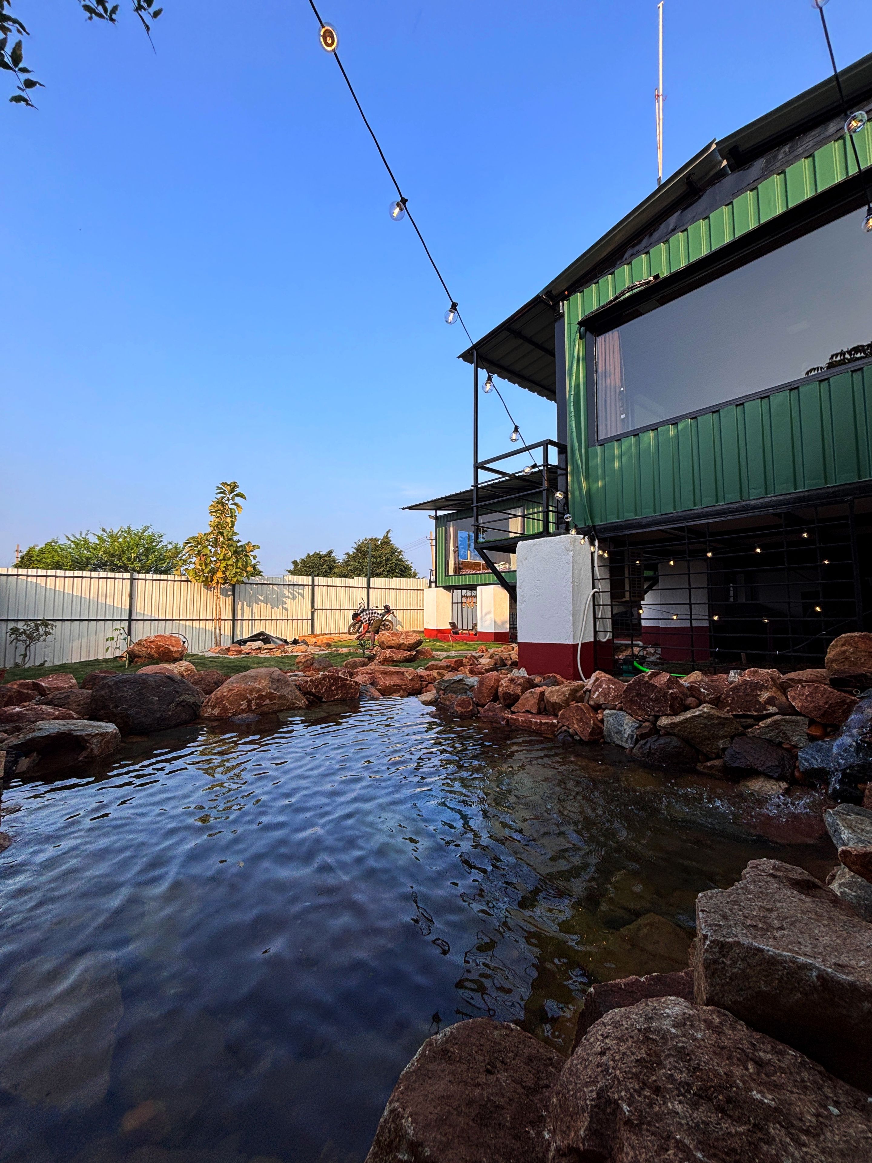 A building with a green facade, a water feature with rocks, and a clear blue sky.
