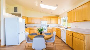 Une cuisine moderne avec des meubles en bois, un réfrigérateur blanc, une table à manger avec des chaises et une fenêtre qui laisse entrer la lumière naturelle.