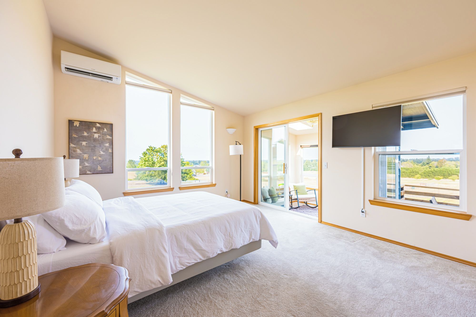 Quarto com cama, TV de tela plana na parede e uma grande janela com vista para áreas verdes.