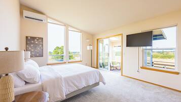 Quarto com cama, TV de tela plana na parede e uma grande janela com vista para áreas verdes.