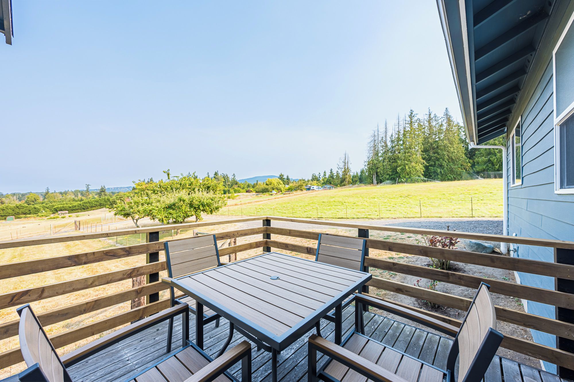 A wooden deck with a table and benches, overlooking a grassy field and trees.