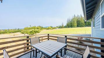 A wooden deck with a table and benches, overlooking a grassy field and trees.