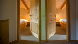 Una habitación con dos puertas de madera que dan a un dormitorio con cama y mesita de noche.
