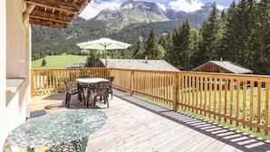 Una terraza de madera con mesa y sillas, con vistas a un paisaje montañoso.