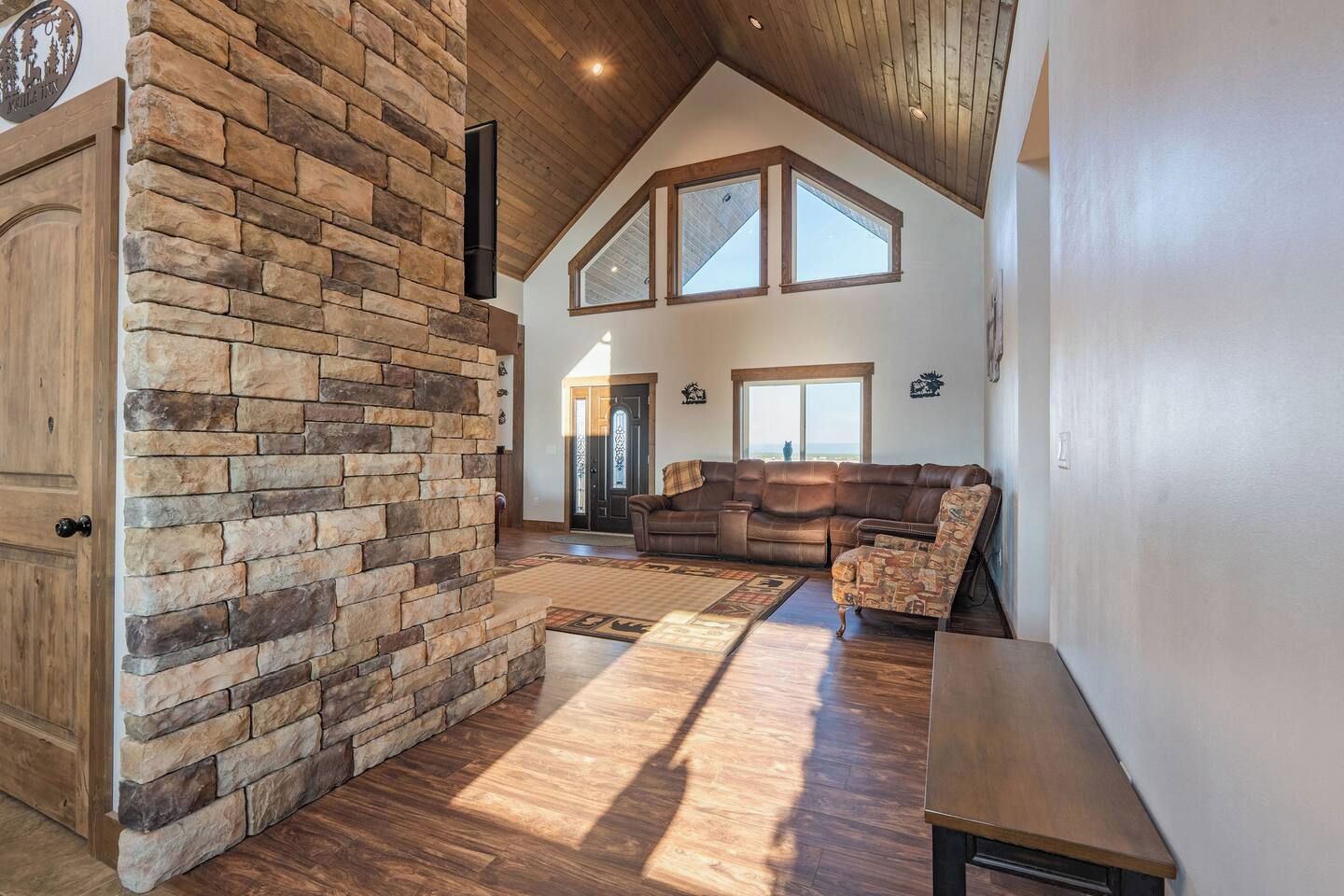 A spacious living area with a stone wall, wooden flooring, a leather sofa, and a large window.
