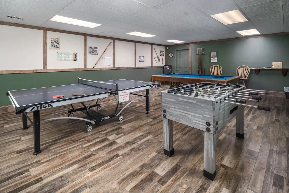 A room with a ping pong table, a foosball table, and a pool table.