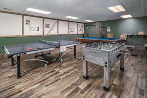 A room with a ping pong table, a foosball table, and a pool table.