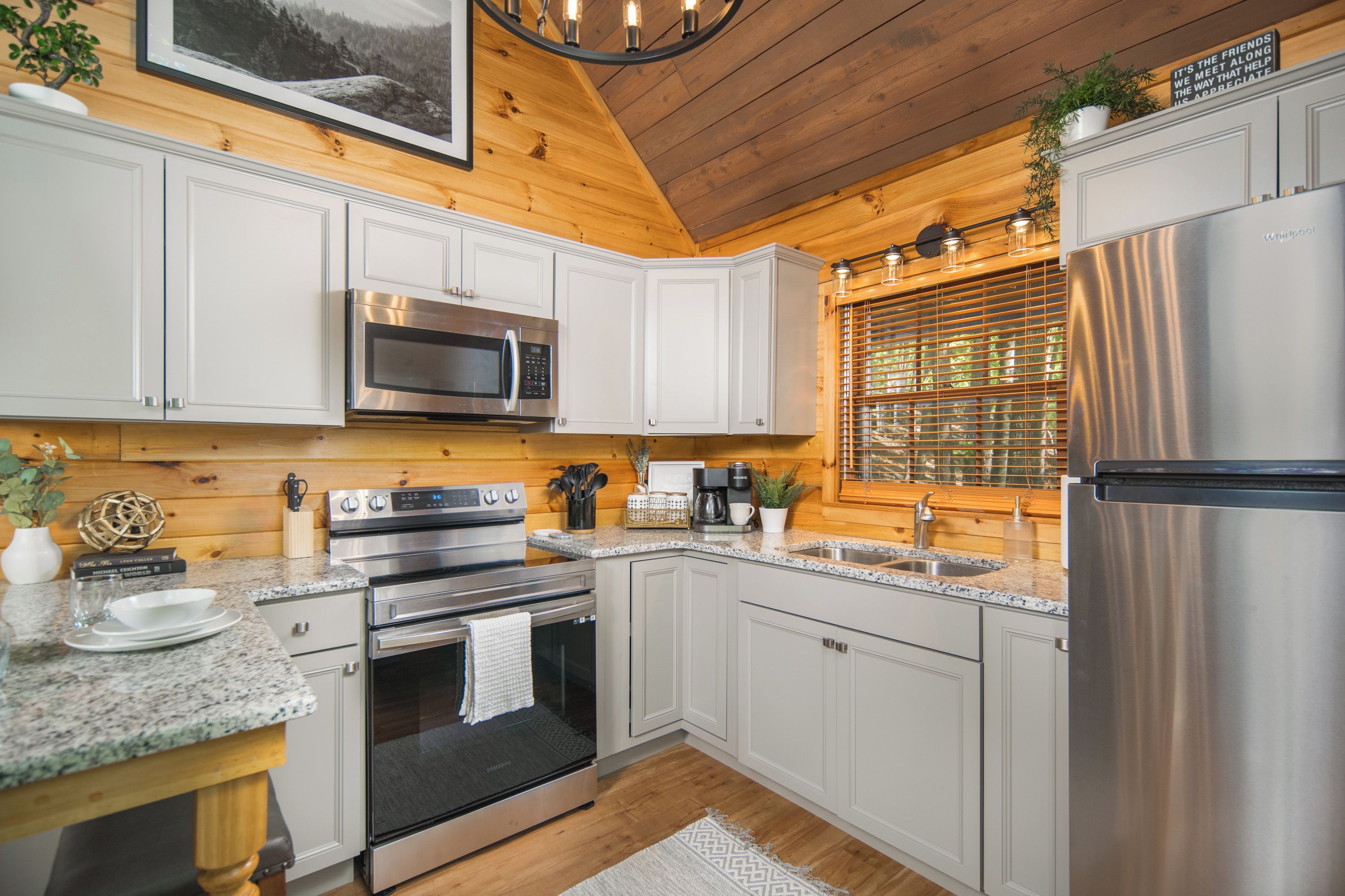 Una cocina moderna con armarios blancos, electrodomésticos de acero inoxidable, encimera de granito y techo de madera.