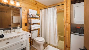 Baño de cabaña de madera con lavamanos blanco, espejo, inodoro y cortina de ducha.