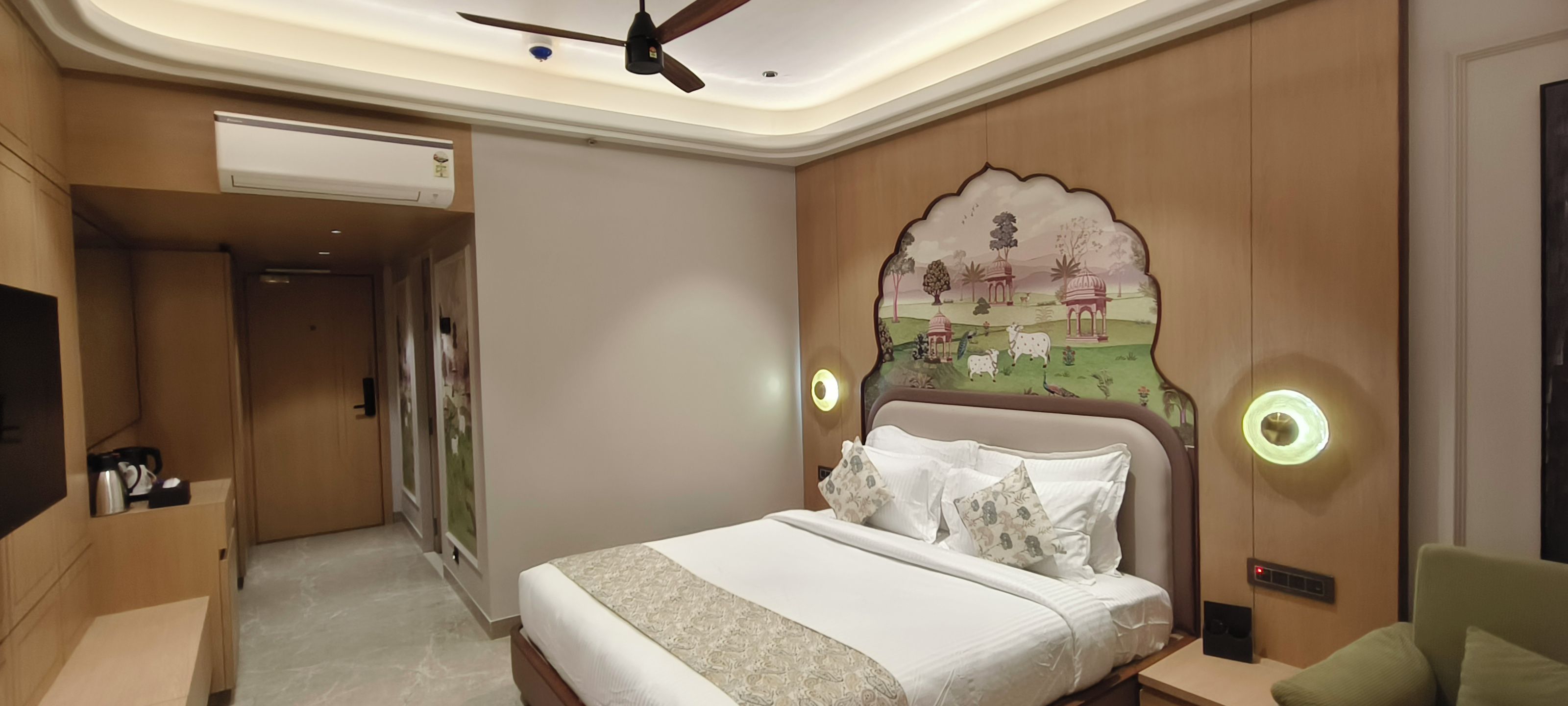 A hotel room with a bed, a flat-screen TV, a ceiling fan, and a decorative wall mural.