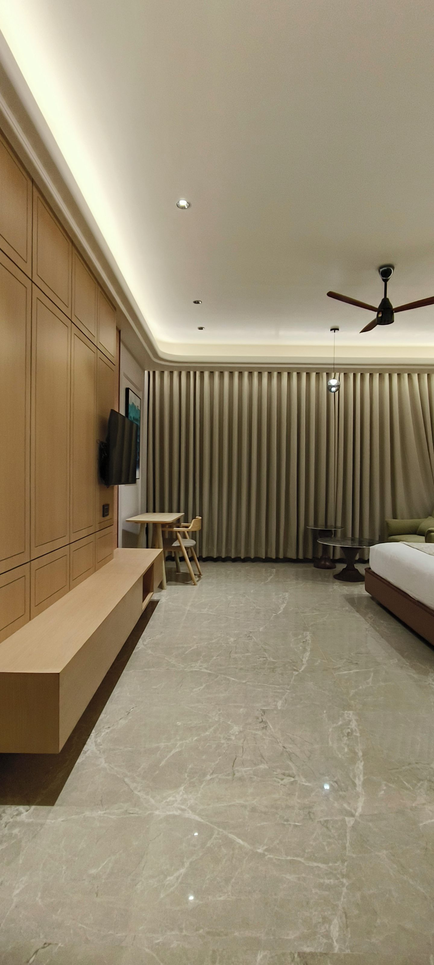 Quarto de hotel moderno com cama, escrivaninha, cadeira, televisão e ventilador de teto.
