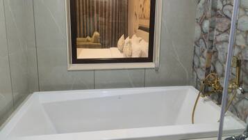 A bathroom with a bathtub, a shower, and a window with a view of a bedroom.