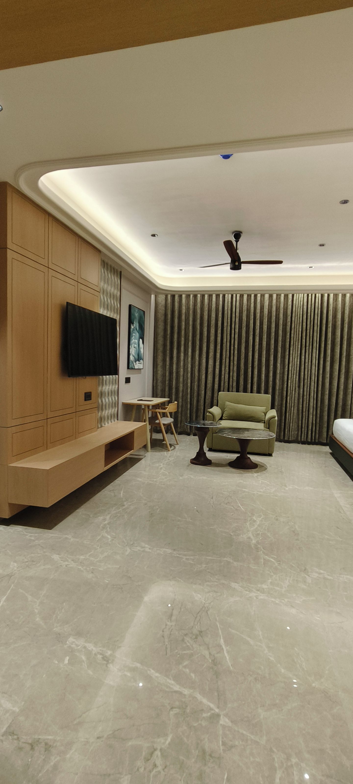 A modern living room with a flat-screen TV mounted on a wooden cabinet, a green sofa, a small round coffee table, and a ceiling fan.