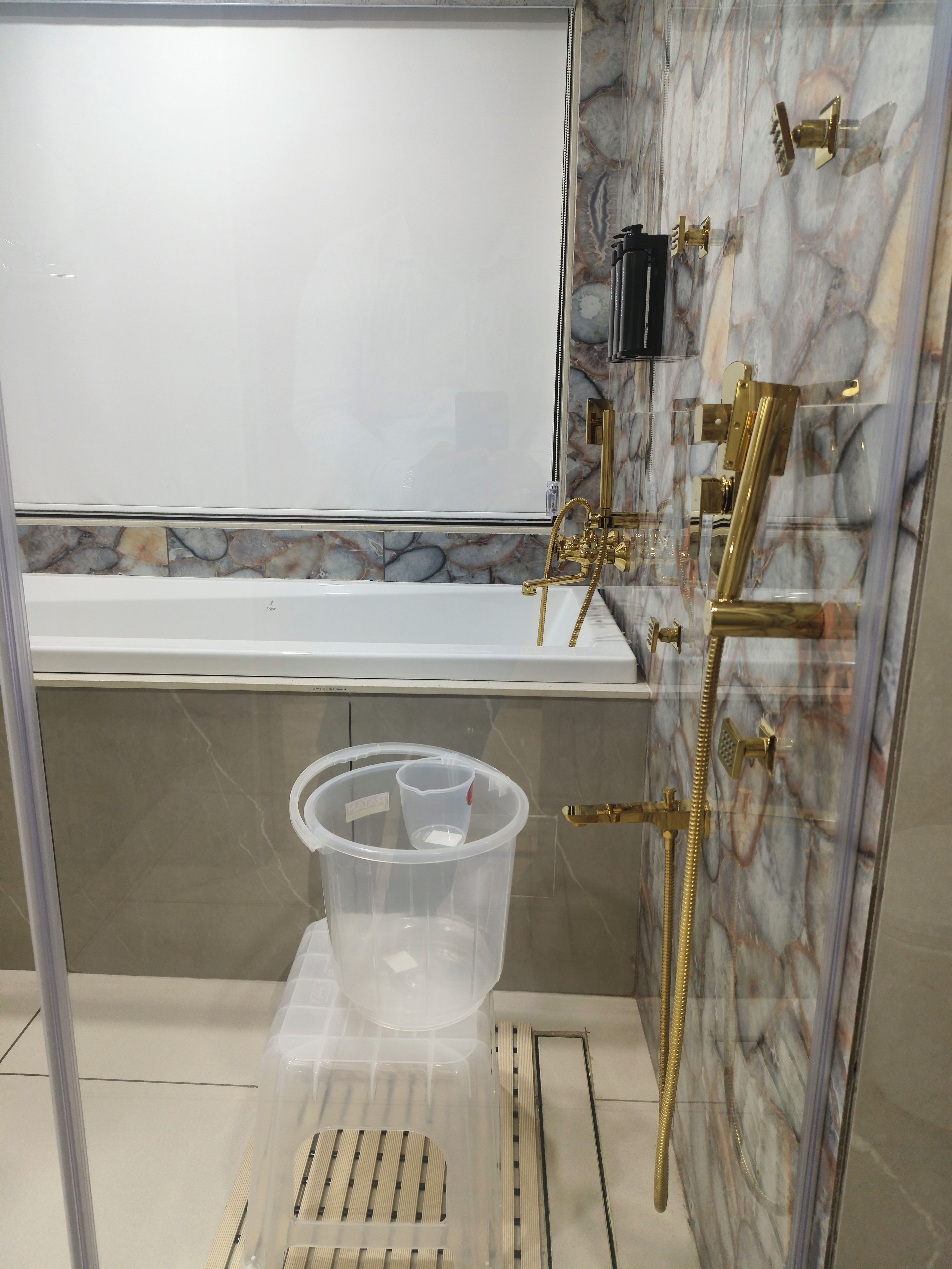 Un bany amb banyera, dutxa amb detalls daurats i un recipient de plàstic transparent a terra.