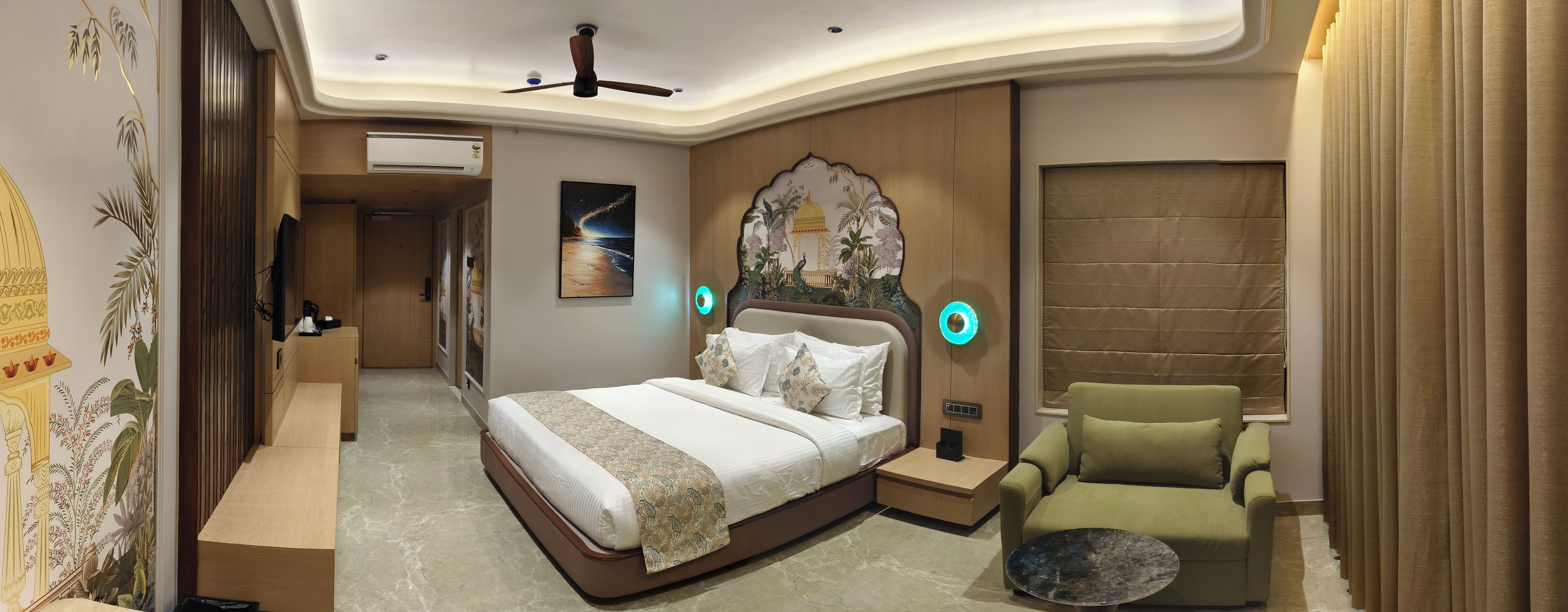 Habitación de hotel con cama, un sillón verde, mesita de noche, unidad de aire acondicionado y una pared decorativa con una escena nocturna.