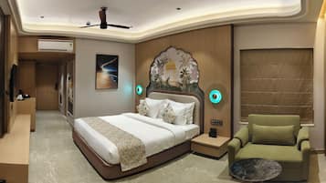 Habitación de hotel con cama, un sillón verde, mesita de noche, unidad de aire acondicionado y una pared decorativa con una escena nocturna.