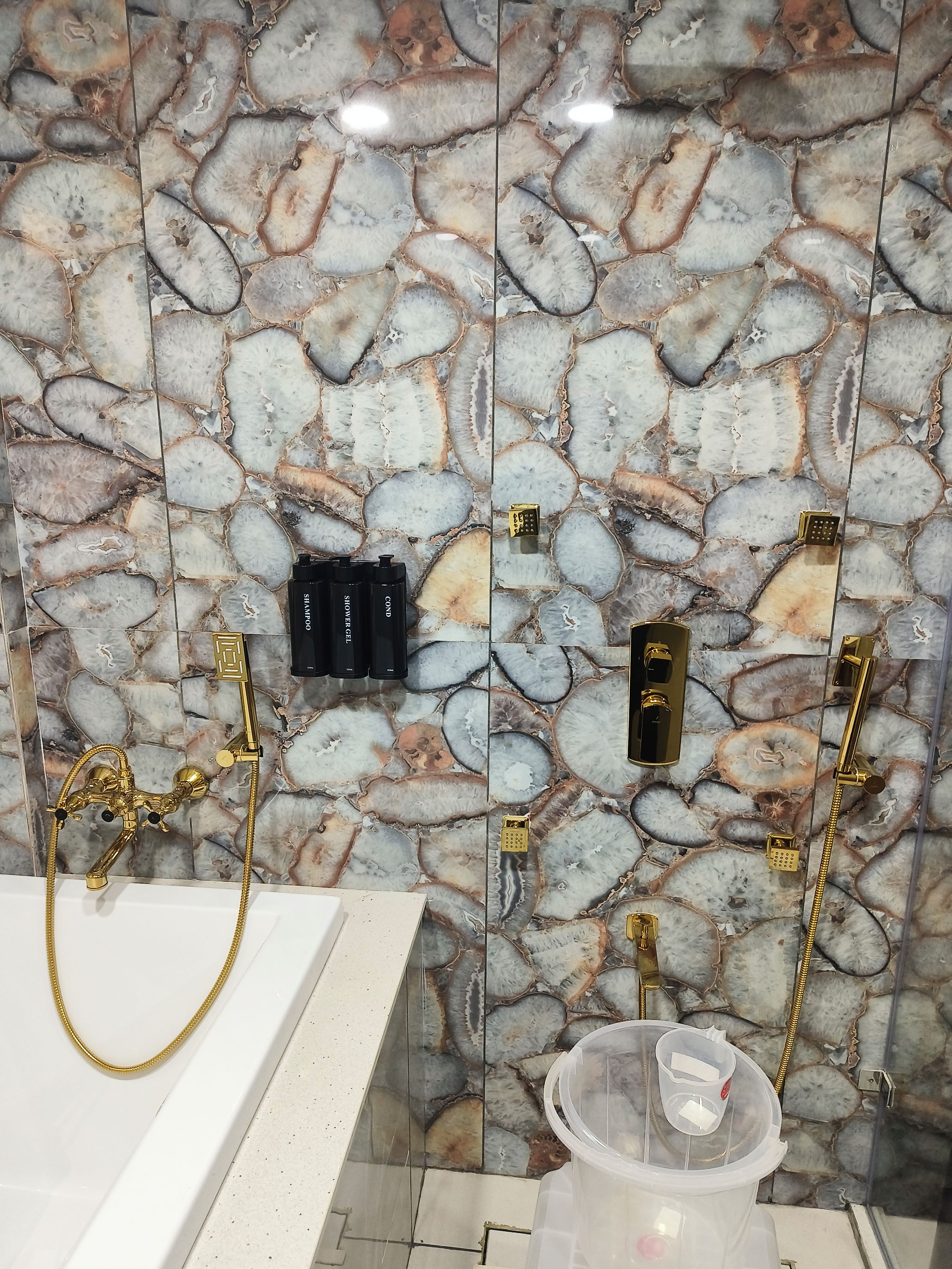 A bathroom with a stone wall, gold fixtures, and a white bathtub.