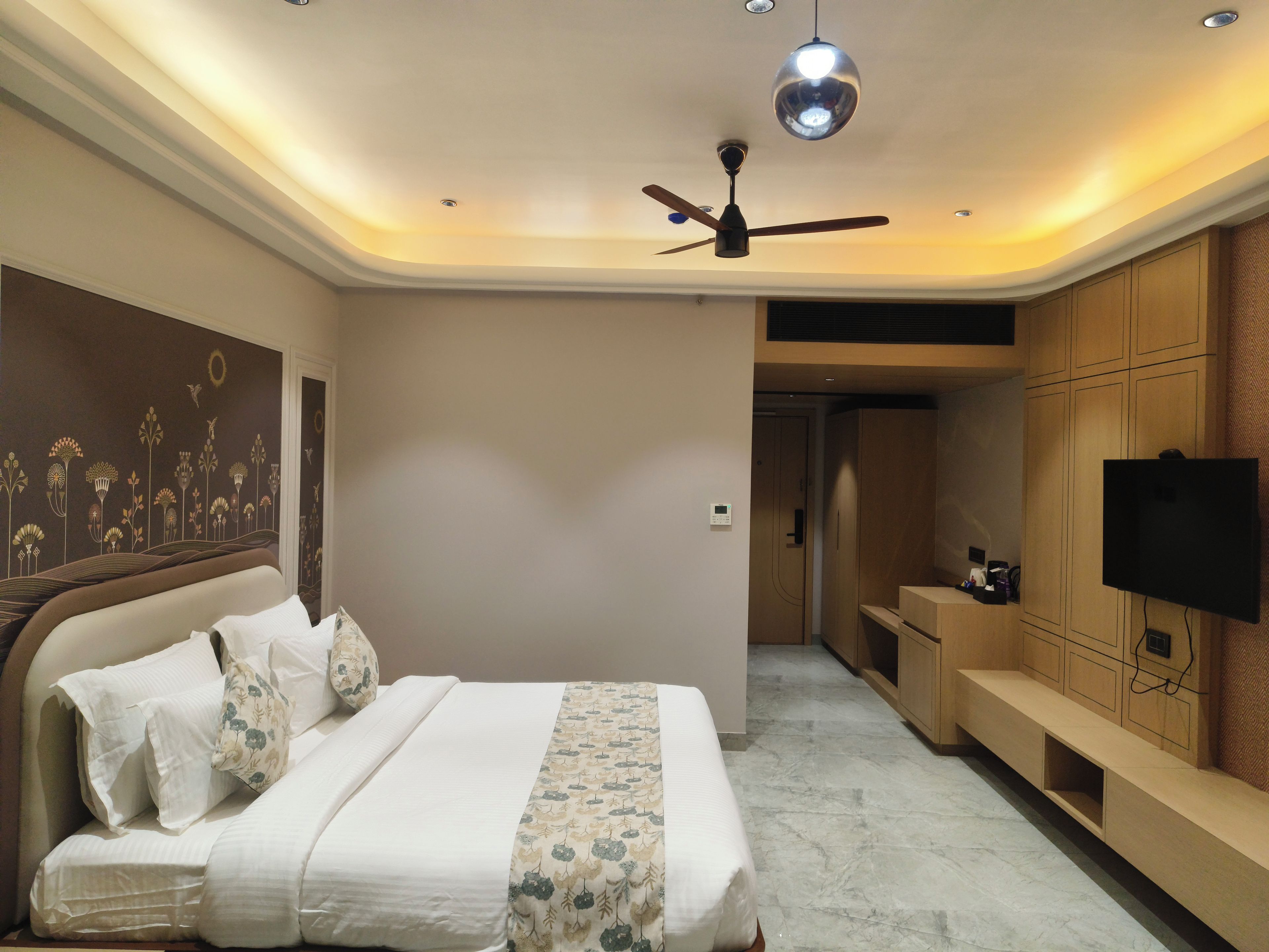 A bedroom with a bed, a ceiling fan, a wall-mounted TV, and a door leading to a bathroom.