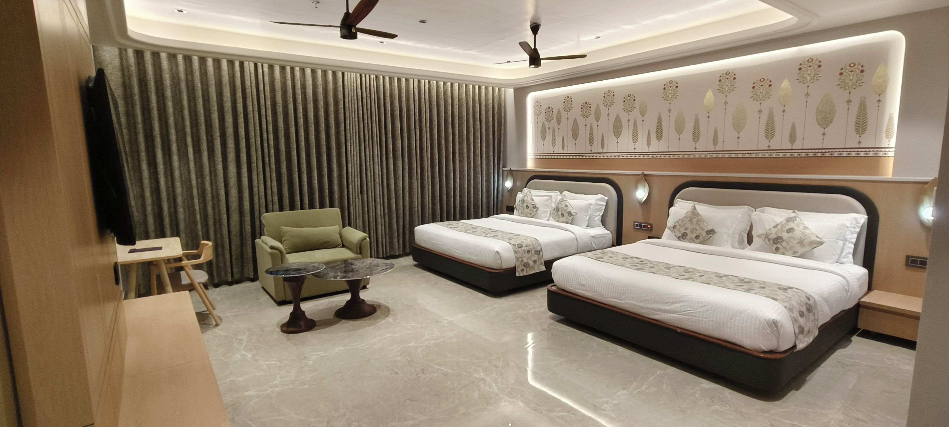 A hotel room with two beds, a sofa, a small table, and a ceiling fan.