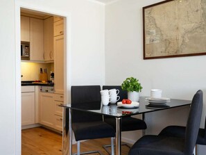 A modern kitchen with white cabinets, a dining table with black chairs, and a potted plant. - Holiday Apartment With 1 Bedroom (Sylt)