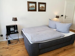 A bedroom with a bed, bedside lamps, a desk with a lamp, and two framed pictures on the wall. - Holiday Apartment With 1 Bedroom (Sylt)