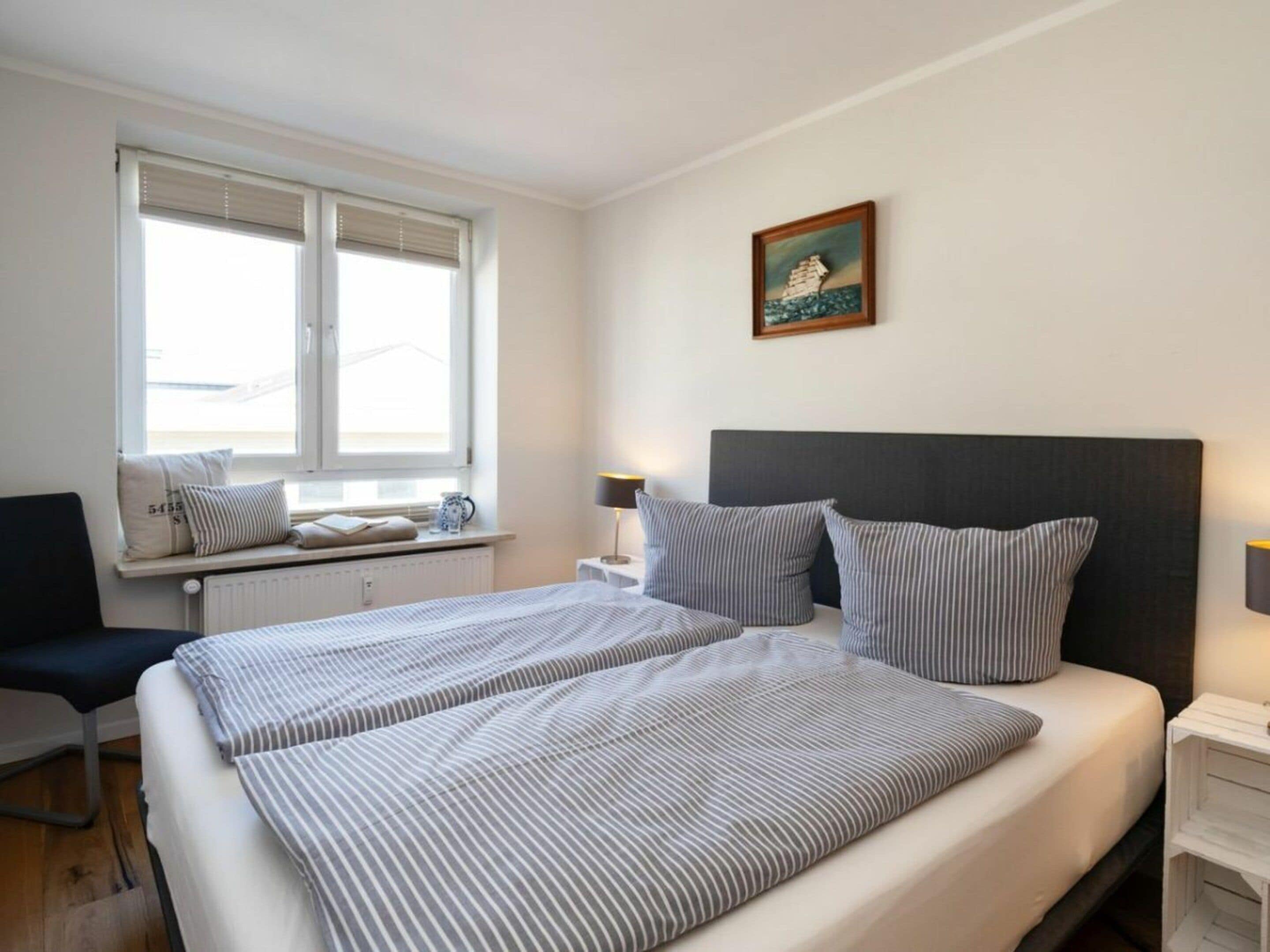 A hotel room with a bed, a window with blinds, a bedside table with a lamp, and a wall-mounted picture.