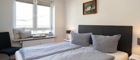 A hotel room with a bed, a window with blinds, a bedside table with a lamp, and a wall-mounted picture.