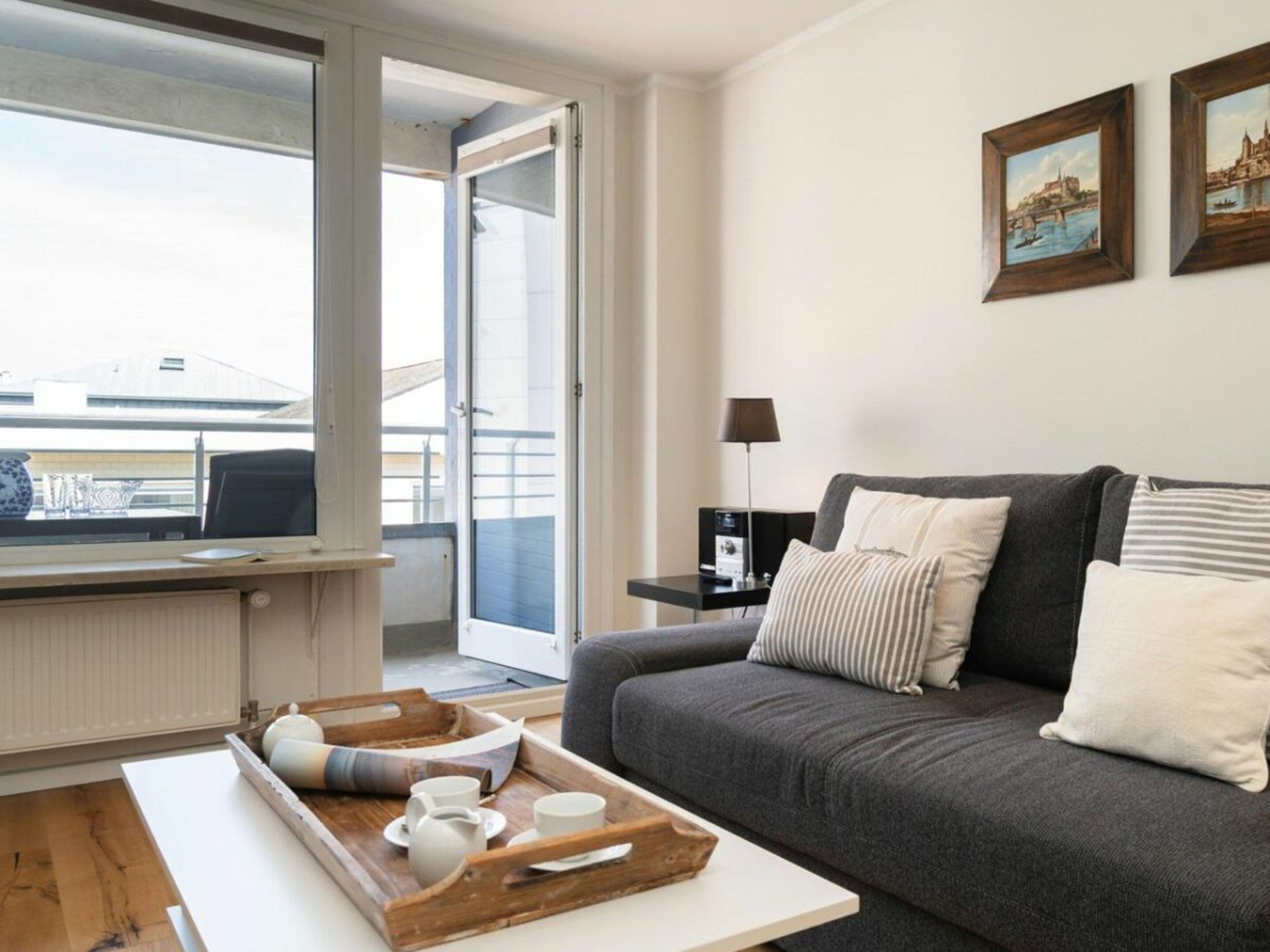 Una sala de estar moderna con un sofá gris, una mesa de centro con una bandeja de objetos, una lámpara y dos cuadros en la pared.